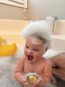 a baby is taking a bath with foam on his head and holding a rubber duck