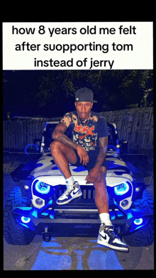 a man in a ac dc shirt sits on the front of a blue and white jeep