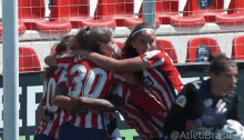 a group of women are hugging each other on a soccer field . one of the players has the number 30 on her jersey .