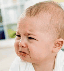 a close up of a baby crying with his mouth open .