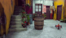 a wooden barrel sits in the middle of a courtyard next to a red tricycle