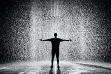 a man is standing in the rain with his arms outstretched in a room .