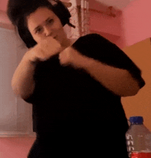 a woman wearing headphones and a black shirt is standing in front of a pink wall .