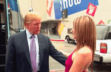 a man in a suit and tie is talking to a woman in a red dress in front of a sign that says show