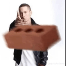 eminem is holding a brick in his hand and pointing at it .