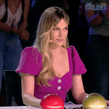 a woman in a purple dress is sitting at a table with a microphone in front of a sign that says spain talent