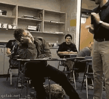 a group of people are sitting at desks in a classroom with a man standing in front of them .