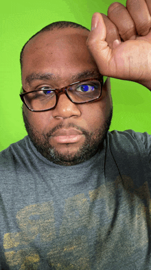 a man wearing glasses and a gray shirt holds his fist up in front of his face