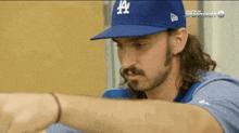 a man wearing a la dodgers hat is looking at his watch