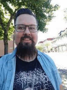 a man with a beard and glasses is wearing a blue shirt and a black t-shirt .