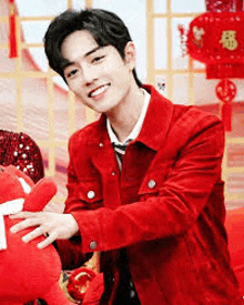 a man in a red jacket is holding a stuffed animal and smiling .