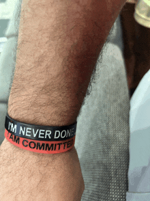 a man has a bracelet on his wrist that says i 'm never done i am committed