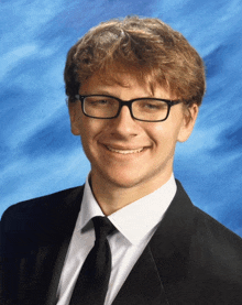 a young man wearing glasses and a suit and tie smiles for the camera