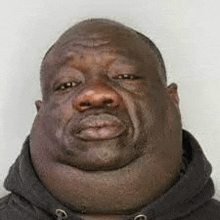 a man with a very large neck and a black hoodie is making a funny face .