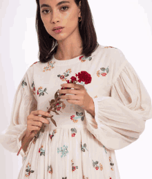 a woman in a white dress holds a red flower in her hand