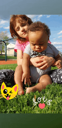 a little girl is holding a baby in her arms and the word love is written in the grass