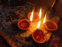 four candles are lit on a table with a patterned cloth