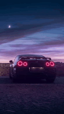 a black sports car is parked on a dirt road with a purple sky in the background