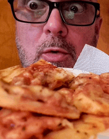 a man with glasses and a beard is looking at a pizza