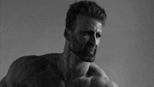 a shirtless man with a beard looks at the camera in a black and white photo