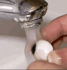 a person is washing an eye in a sink with water running from a faucet .