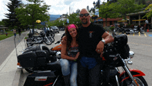 a man and a woman are posing for a picture in front of a harley davidson motorcycle