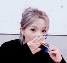 a woman with long blue nails is eating a piece of food