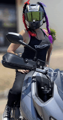 a woman wearing a helmet and a triumph tank top sits on a motorcycle