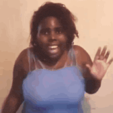 a woman in a blue tank top is smiling and waving her hand .