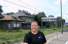 a man in a black nike shirt stands in front of a radzymin sign