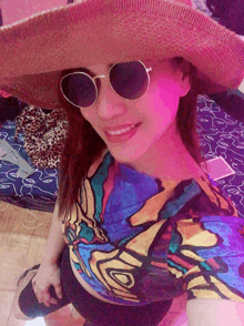 a woman wearing a hat and sunglasses is smiling and wearing a colorful shirt