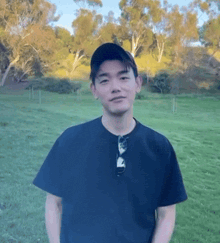 a young man wearing a black shirt and a hat stands in a field