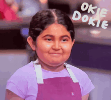 a little girl wearing a purple apron and a purple shirt is smiling and says okie dokie