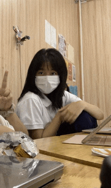 a girl wearing a face mask is giving a peace sign in a classroom