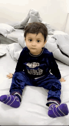 a little boy is sitting on a bed wearing purple socks and a teddy bear shirt