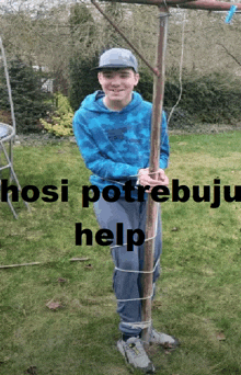 a boy in a blue sweatshirt is tied to a pole with the words " hosi potrebuju help " written below him