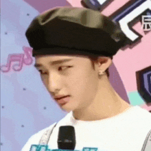 a young man wearing a beret and earrings is talking into a microphone .