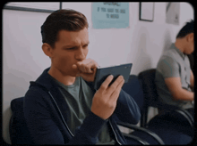 a man sitting in a waiting room with a sign on the wall that says please