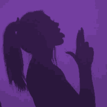 a shadow of a woman with a ponytail sticking her tongue out against a purple background .