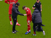 a soccer player is being helped on the field by a man wearing a jacket that says ' liverpool ' on it