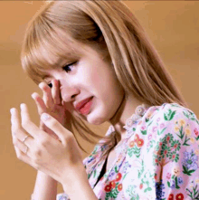 a woman is covering her face with her hands while wearing a floral shirt .