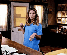 a woman in a blue scrub top is standing behind a counter in a room .