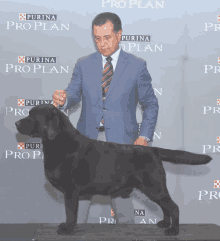 a man in a blue suit stands next to a black dog in front of a purina pro plan sign