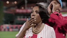 a woman in a baseball uniform is covering her mouth with her hand while a man shouts .