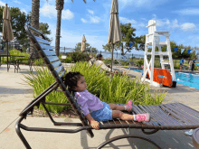 a little girl sits on a chair near a lifeguard stand