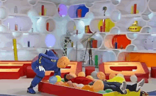 a man is laying on a bed of balloons in a room with a mascot in a blue suit .