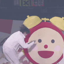 a man in a white shirt stands next to a large red and yellow alarm clock with a smiling face on it