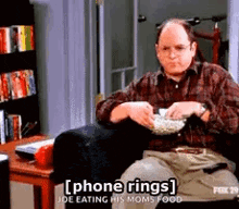 a man in a plaid shirt is sitting in a chair eating popcorn .