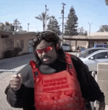 a man wearing a red vest and sunglasses is standing in front of a parking lot .