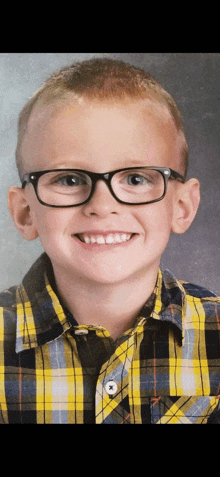 a young boy wearing glasses and a yellow plaid shirt smiles for the camera